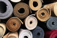 Zbliżenie na gęsto ułożone rolki wykładzin, ukazuje bogactwo faktur oraz zróżnicowaną paletę kolorów