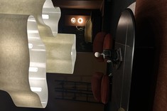 Strefa wypoczynkowa i kawowa w showroomie Metaforma Design. W centrum uwagi duża lampa emanująca ciepłym światłem, w otoczeniu wnętrza w klimacie ‘warm dark elegance’, podkreślającego zarówno głębię, jak i przytulność przestrzeni.